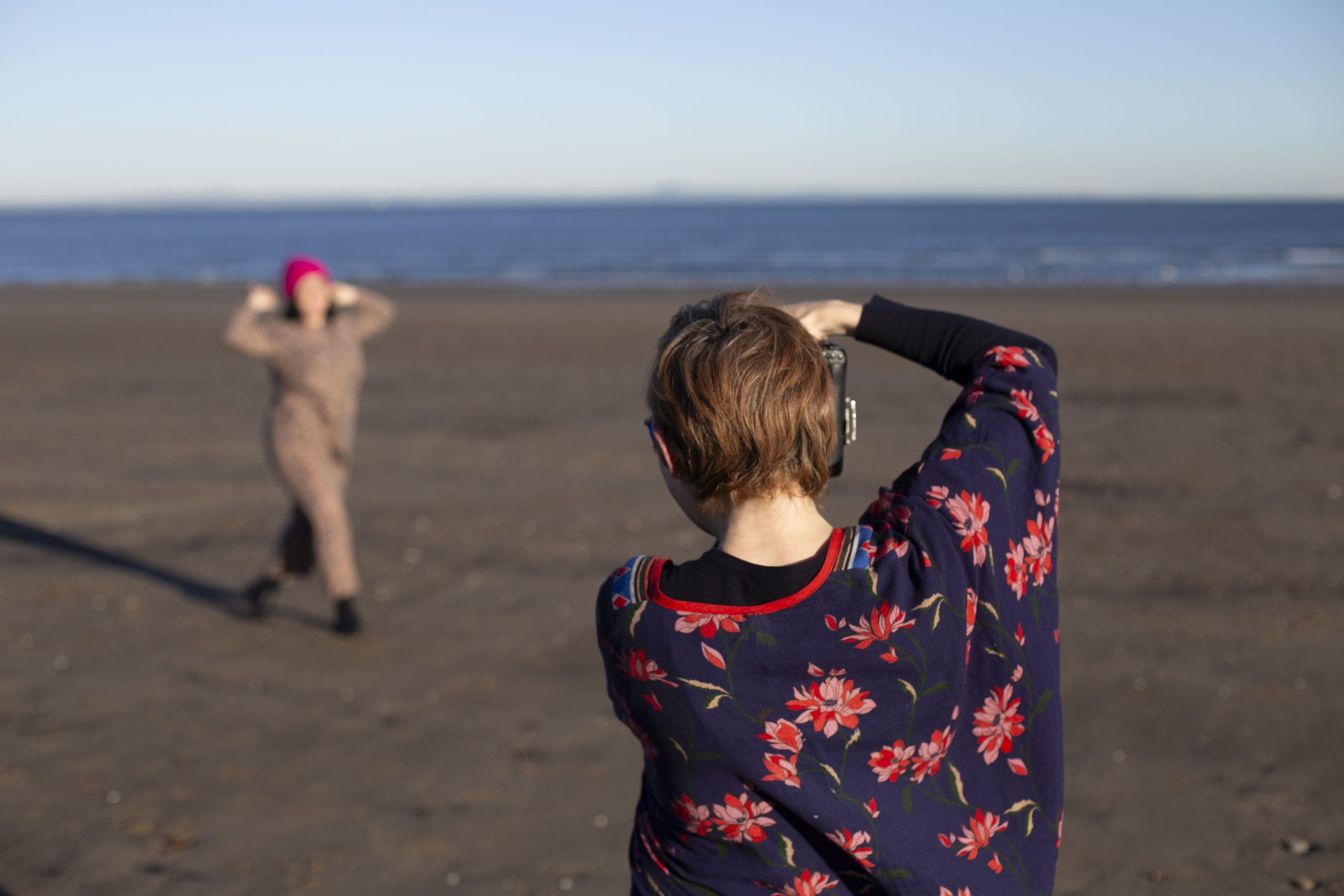 photographer takes a photo of a lady in a pink hat and jumpsuit dancing on the beach