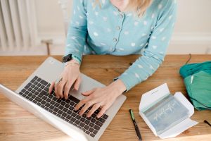 close up of woman typing on a laptop wearing light blue cardigan with white spots