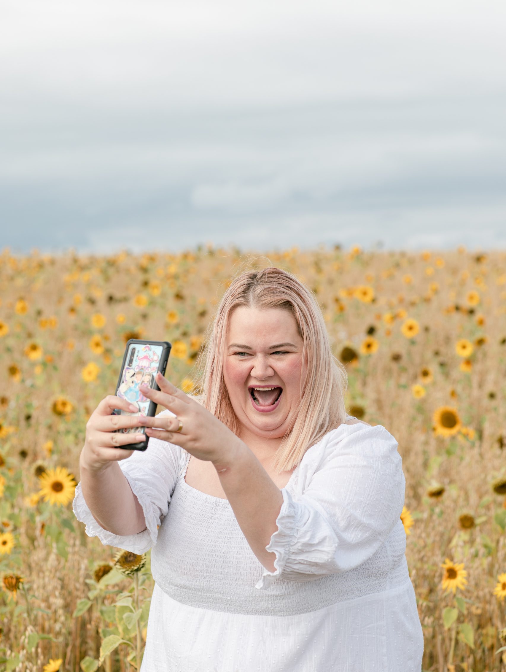 lady in a white dress in a sunflower field taking a selfie