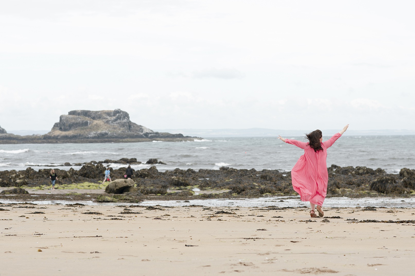 lady in a long pink dress with her hands in the air dancing on the beach