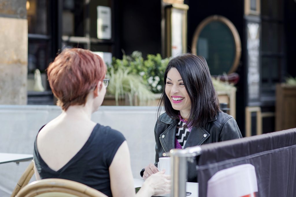 two women laughing over coffee outside