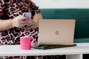 brand photograph - a close up of a laptop with a woman on her phone behind it