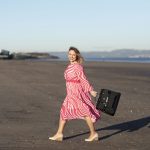 lady walking along a beach on a sunny day swinging her handbag
