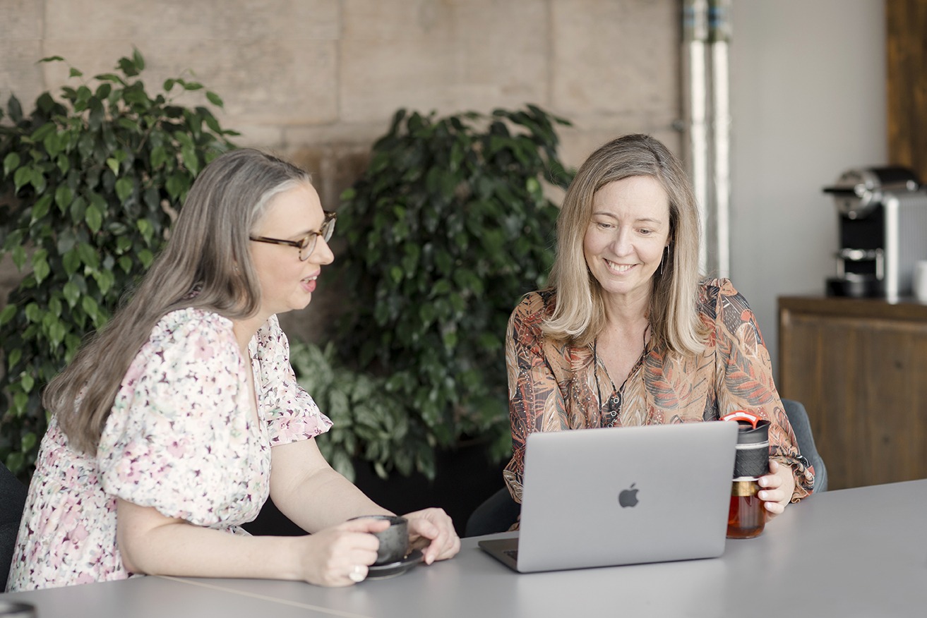two smiling business ladies talk over a lap top