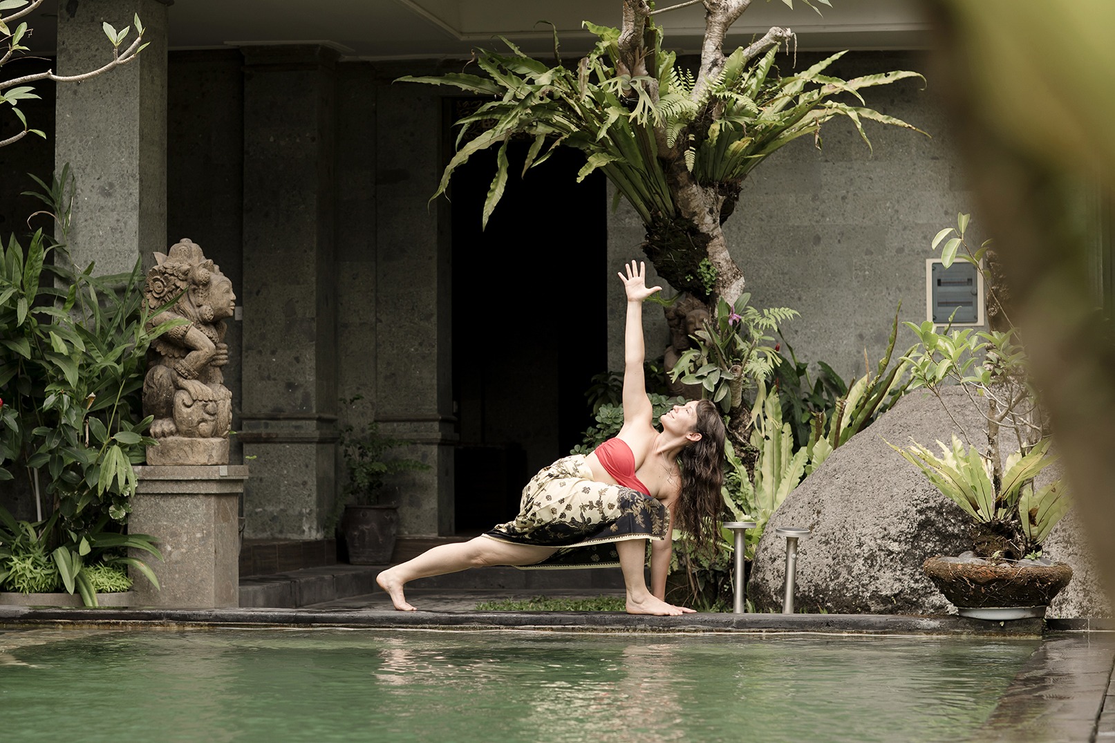 portrait of a lady laughing as she does warrior pose beside a swimming pool at a yoga retreat in Bali