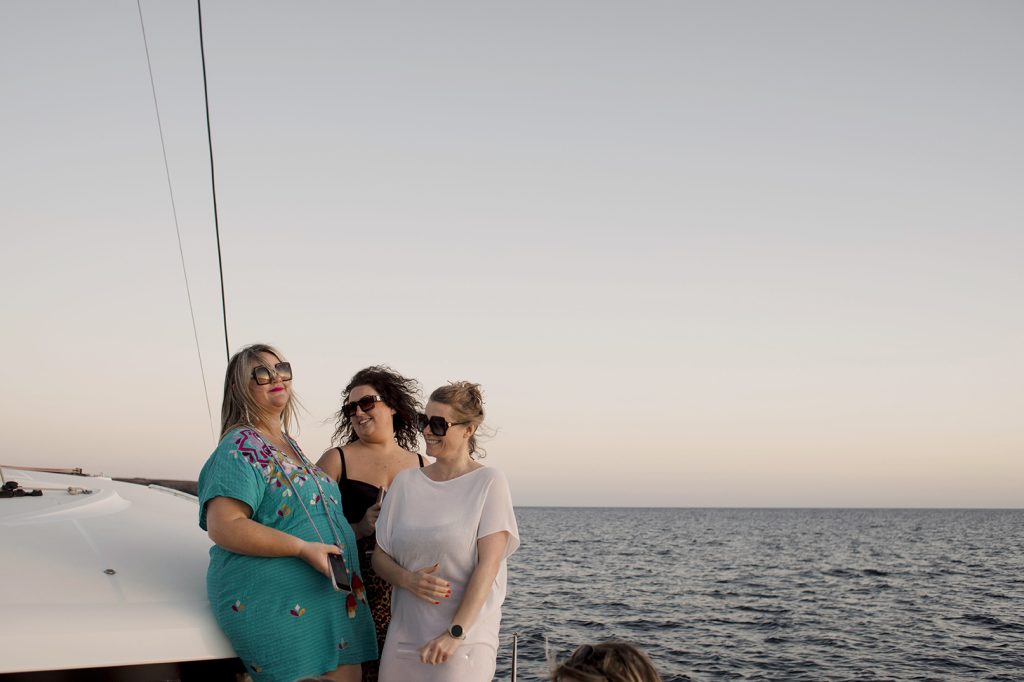 three women on a yacht with a sunset sky