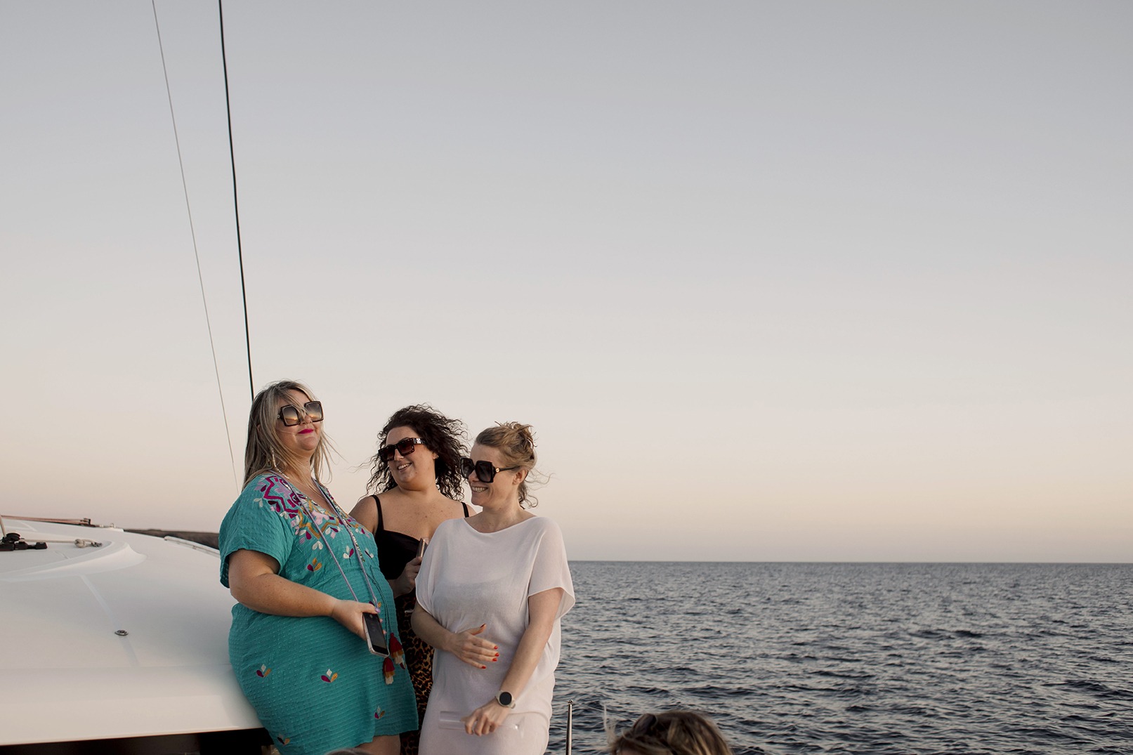 three women on a yacht with a sunset sky