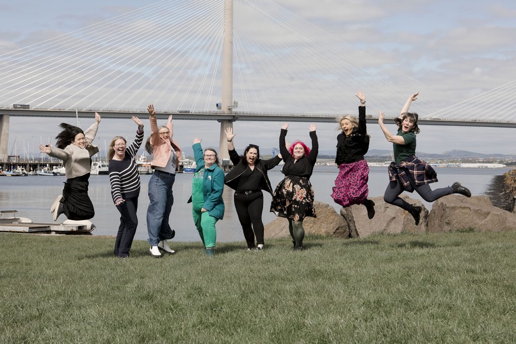 A group of business ladies jumping up in front of a bridge