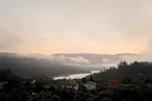 image shows an early morning view over a Portugese valley with mist rising above the water surrounded by hills