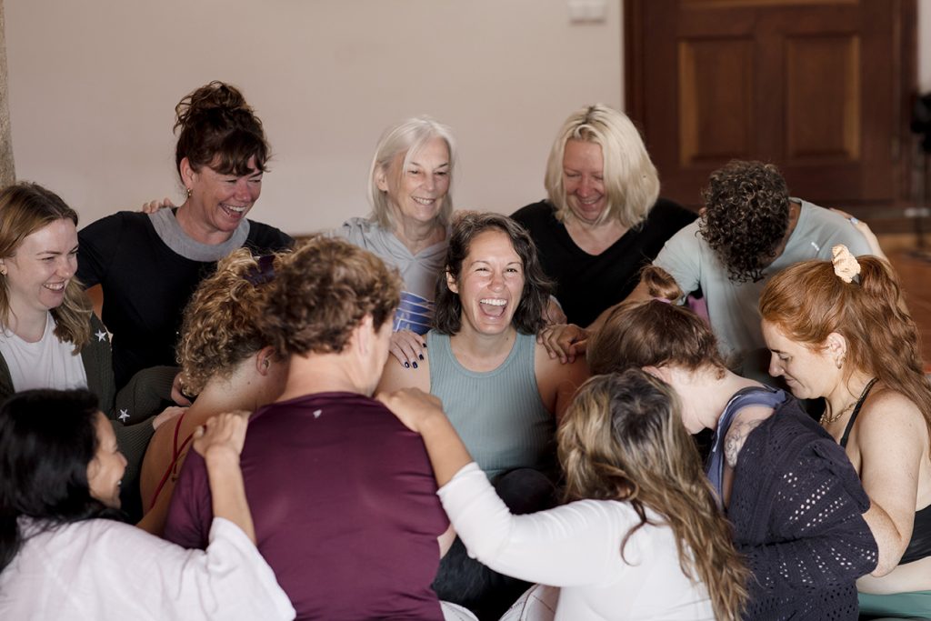 image shows a yoga retreat leader surrounded by students laughing together after practice.