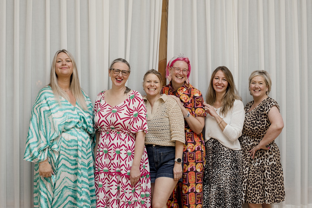 group of business owners on a sales retreat in lanzarote - they are standing against a white curtain smiling and laughing