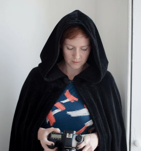 images shows susan the brand photographer wearing a Traitors style cloak while holding and looking down at her camera