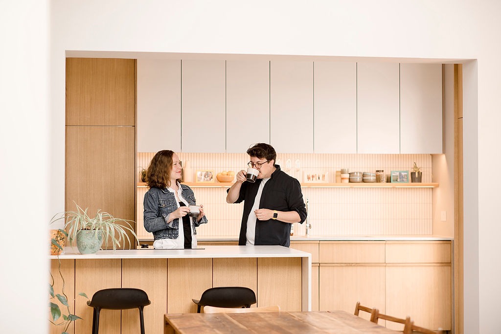a couple stand in an architecturally beautiful kitchen drinking coffee and looking at each other