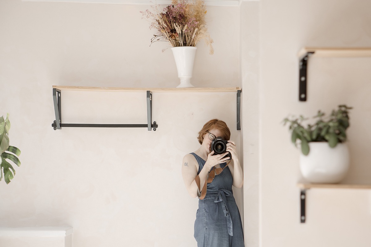 female photographer stands against a wall taking a photograph